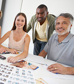 A diverse group of professionals collaborating at a table, reviewing design layouts and photographs.