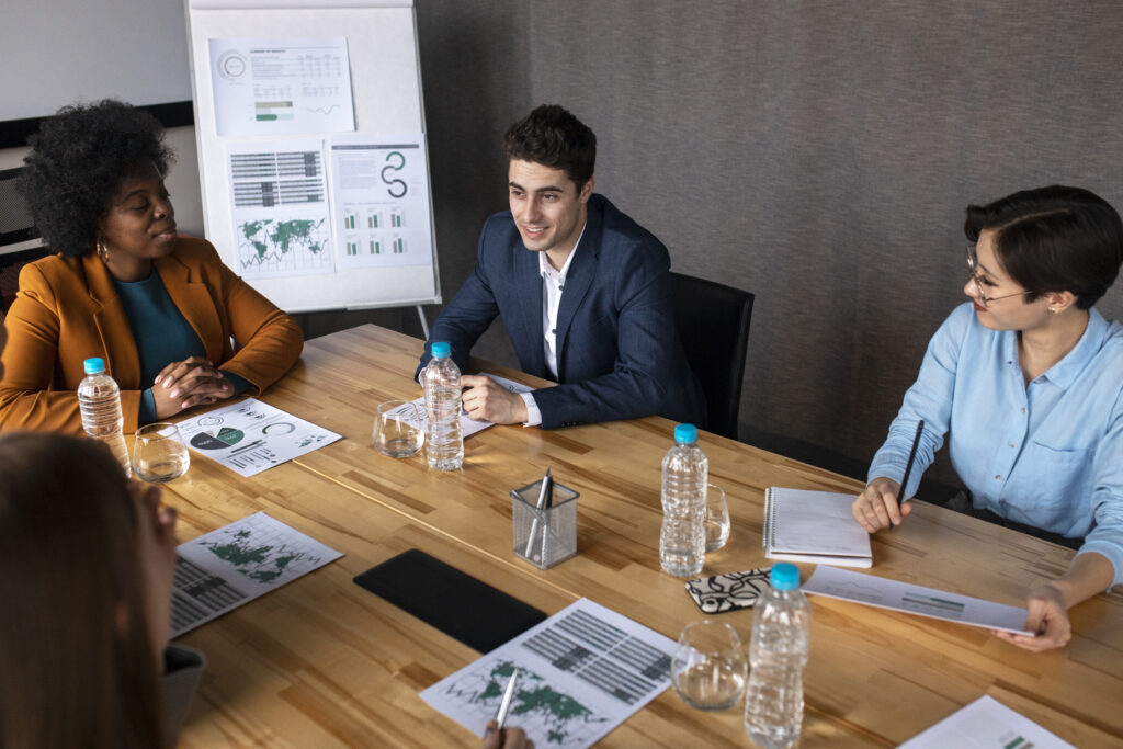 A diverse group of professionals engaged in a business meeting around a conference table with charts and water bottles.